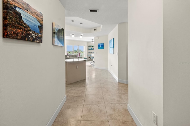 hall with a tray ceiling and light tile flooring