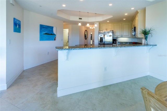 kitchen with pendant lighting, stainless steel appliances, light tile floors, dark stone counters, and a raised ceiling