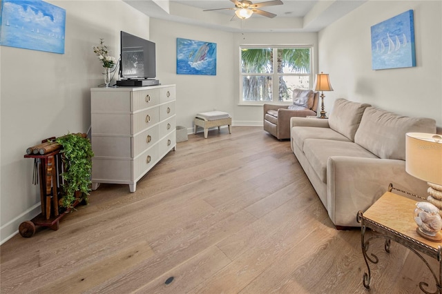 living room featuring light hardwood / wood-style floors, ceiling fan, and a tray ceiling