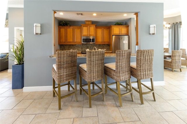 kitchen with light tile floors, tasteful backsplash, a breakfast bar area, appliances with stainless steel finishes, and light stone counters