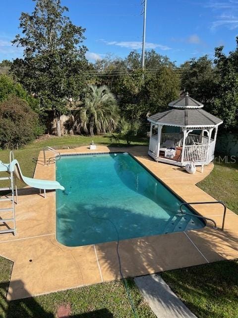 view of swimming pool featuring a gazebo, a water slide, a diving board, and a patio