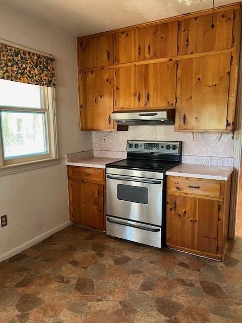 kitchen with backsplash, under cabinet range hood, stainless steel electric stove, brown cabinetry, and stone finish floor