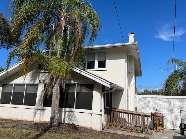 view of side of home featuring stucco siding, a chimney, and a sunroom