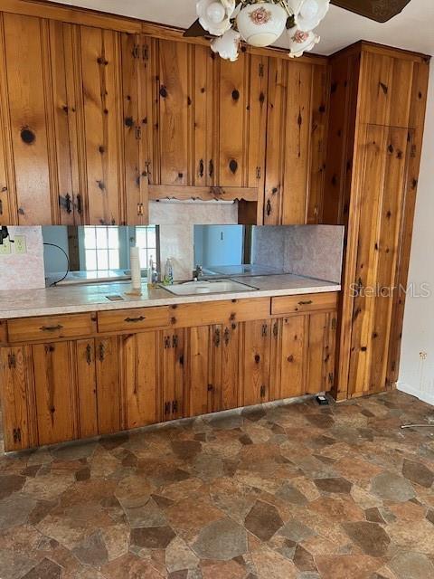 kitchen featuring a sink, stone finish floor, brown cabinetry, and ceiling fan