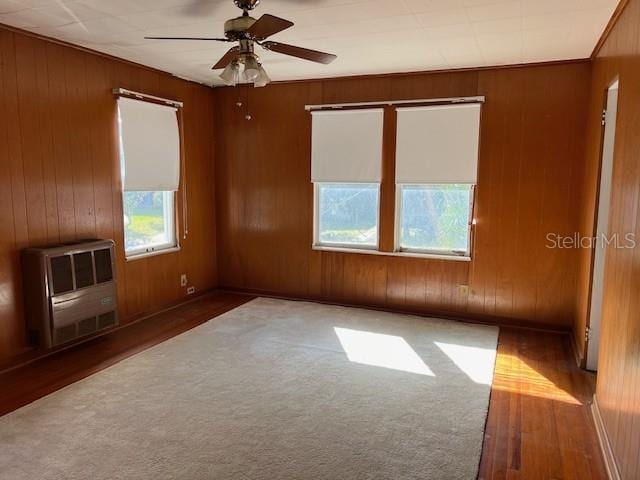 empty room featuring wooden walls, heating unit, and a ceiling fan