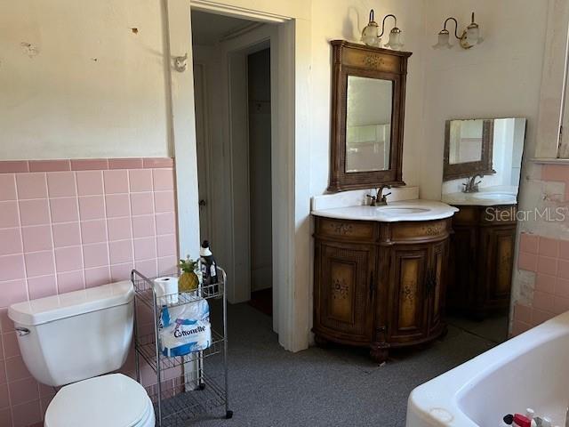 full bath featuring toilet, tile walls, vanity, and a washtub