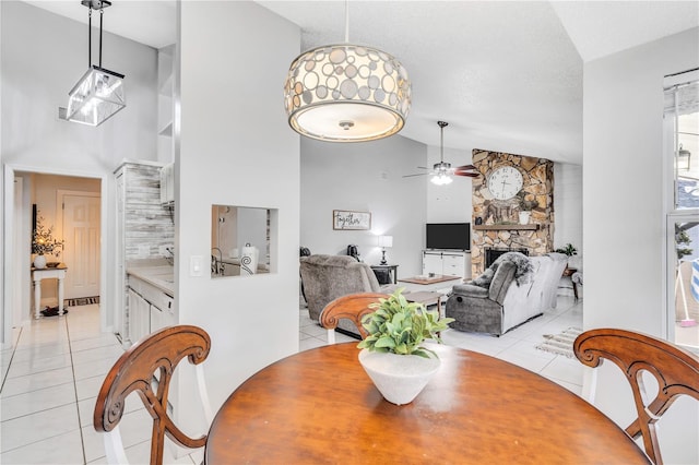 tiled dining room with ceiling fan, high vaulted ceiling, a textured ceiling, and a fireplace