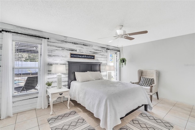 bedroom featuring a textured ceiling, ceiling fan, wood walls, and light tile floors