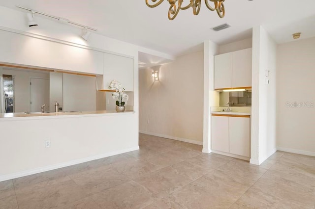 unfurnished living room with light tile floors, track lighting, a chandelier, and sink