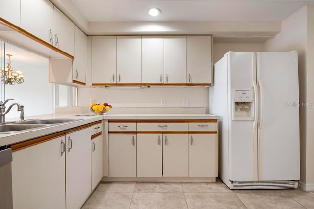 kitchen with sink, light tile floors, white cabinets, white refrigerator with ice dispenser, and an inviting chandelier