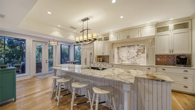 kitchen featuring decorative light fixtures, an island with sink, sink, light stone countertops, and light hardwood / wood-style flooring