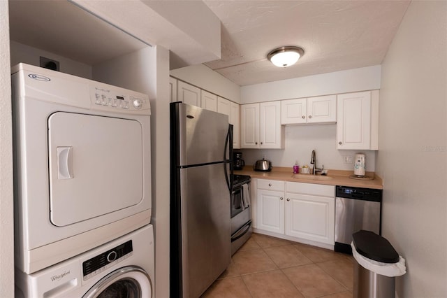 kitchen with stacked washer and dryer, light tile flooring, sink, stainless steel appliances, and white cabinets