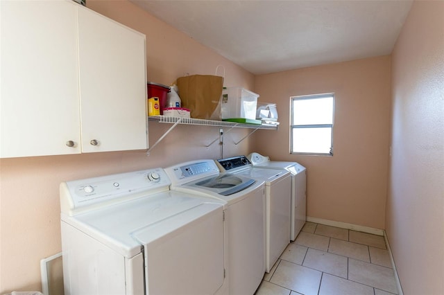 clothes washing area featuring light tile floors, cabinets, and separate washer and dryer