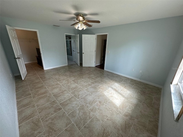 unfurnished bedroom featuring a walk in closet, a closet, ceiling fan, and light tile floors