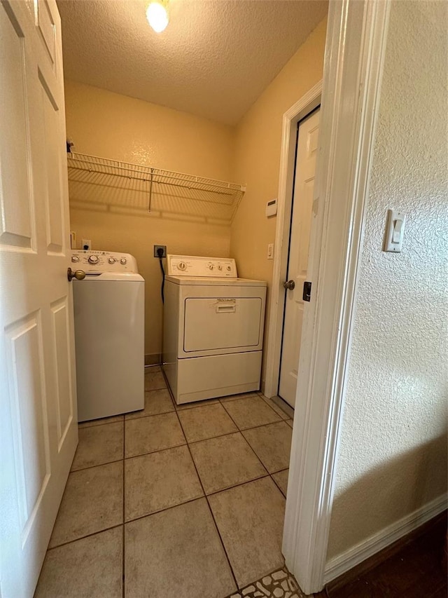 washroom featuring electric dryer hookup, light tile floors, a textured ceiling, and washer and clothes dryer