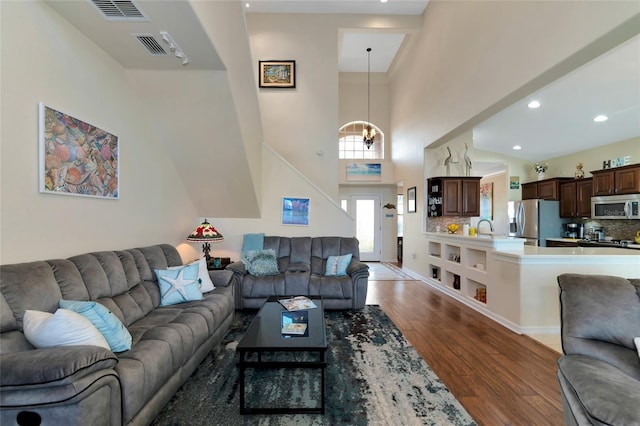 living room featuring a towering ceiling, a notable chandelier, sink, and hardwood / wood-style flooring