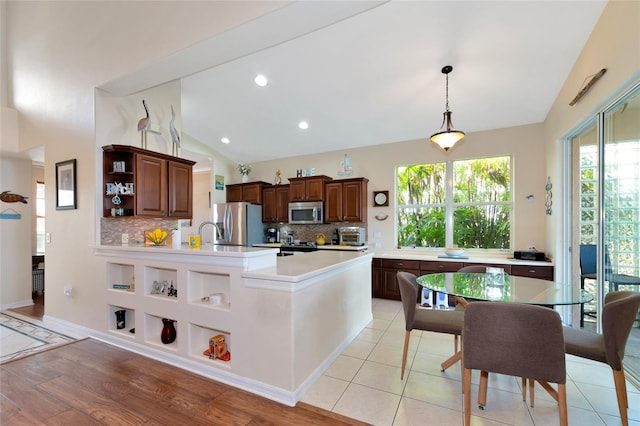 kitchen featuring stainless steel appliances, light tile floors, decorative light fixtures, tasteful backsplash, and a center island with sink