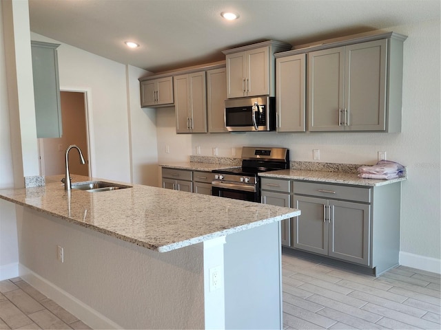 kitchen with kitchen peninsula, light stone counters, stainless steel appliances, sink, and gray cabinets