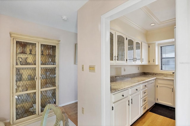 bar featuring sink, light stone counters, white dishwasher, light wood-type flooring, and ornamental molding