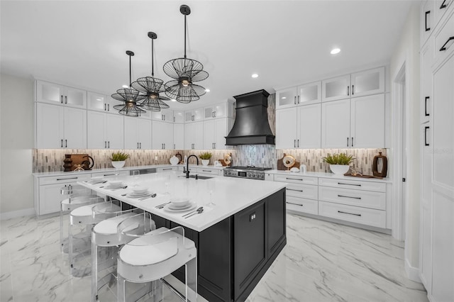 kitchen featuring decorative light fixtures, an island with sink, light tile floors, custom range hood, and tasteful backsplash