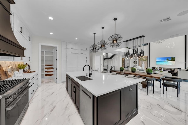 kitchen with premium range hood, decorative light fixtures, appliances with stainless steel finishes, a kitchen island with sink, and sink