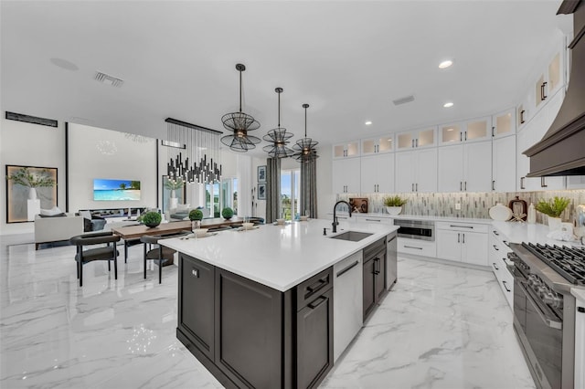 kitchen featuring an island with sink, sink, light tile floors, hanging light fixtures, and stainless steel appliances