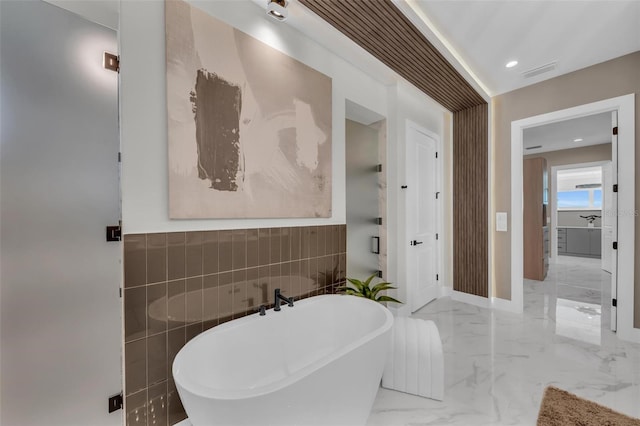 bathroom with tile walls, a bath to relax in, and tile flooring