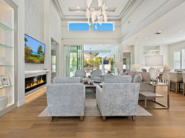 living room featuring a high ceiling, a notable chandelier, light hardwood / wood-style floors, and a tray ceiling