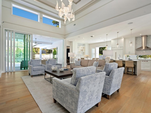 living room with a towering ceiling, sink, light wood-type flooring, and an inviting chandelier