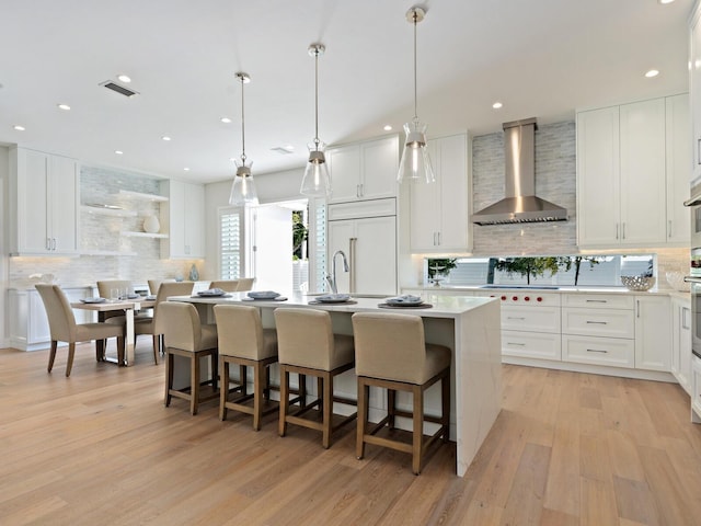 kitchen featuring wall chimney range hood, light hardwood / wood-style floors, tasteful backsplash, and paneled built in refrigerator