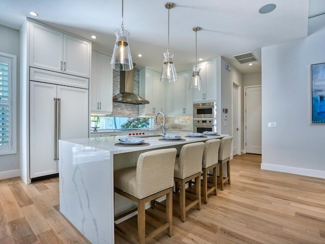 kitchen featuring white cabinets, light hardwood / wood-style floors, wall chimney exhaust hood, and a kitchen island with sink