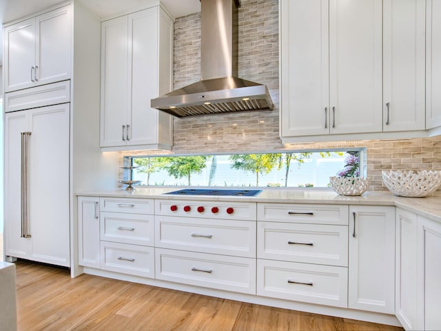 kitchen featuring wall chimney exhaust hood, tasteful backsplash, light hardwood / wood-style floors, and white cabinetry