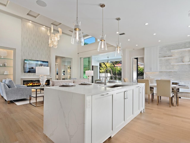 kitchen featuring hanging light fixtures, a large fireplace, sink, light hardwood / wood-style flooring, and white cabinets