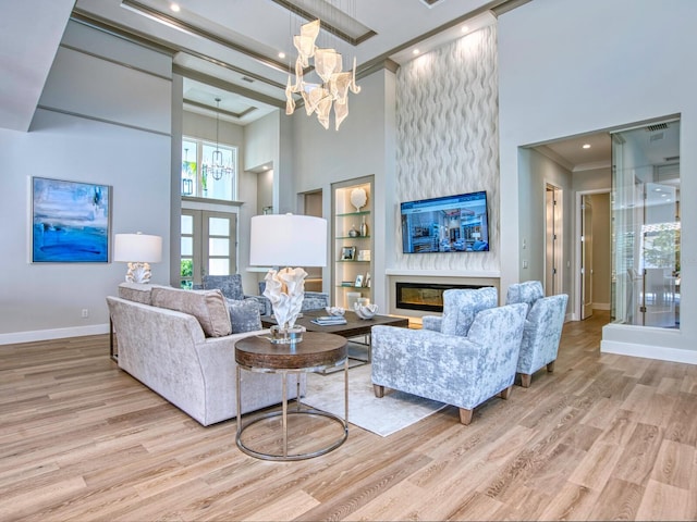 living room featuring a towering ceiling, a notable chandelier, light wood-type flooring, and a fireplace