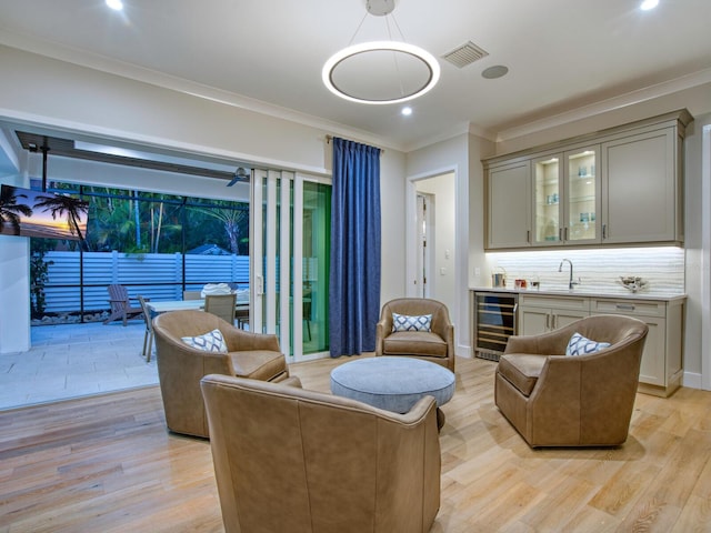 living room featuring wine cooler, ornamental molding, sink, and light hardwood / wood-style flooring