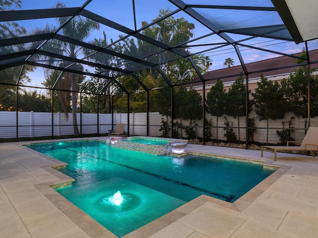 pool at dusk with a patio, an in ground hot tub, a lanai, and pool water feature