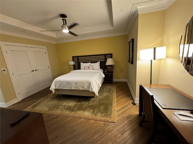 bedroom with dark hardwood / wood-style flooring, a closet, ceiling fan, and a tray ceiling