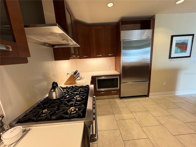 kitchen with built in appliances, wall chimney range hood, light tile flooring, tasteful backsplash, and dark brown cabinetry