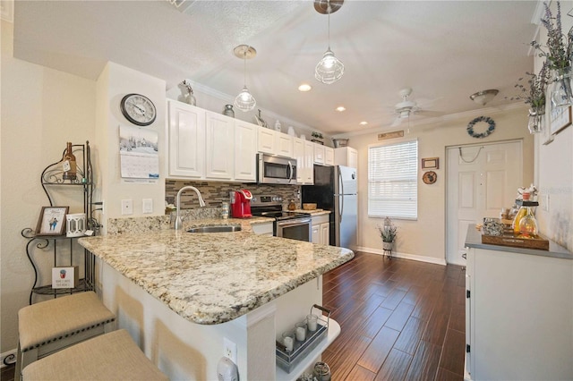 kitchen with appliances with stainless steel finishes, hanging light fixtures, a kitchen breakfast bar, kitchen peninsula, and sink