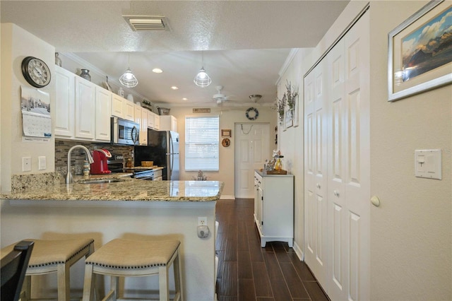 kitchen with light stone counters, white cabinets, hanging light fixtures, kitchen peninsula, and appliances with stainless steel finishes