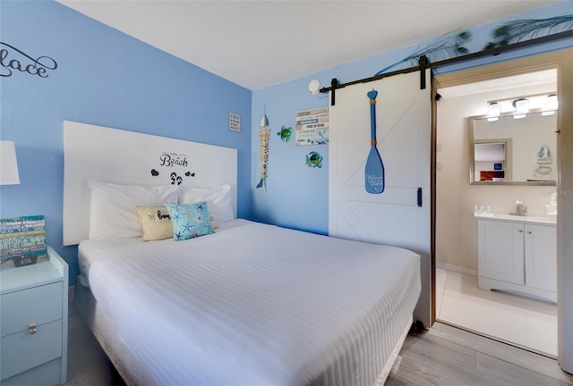 bedroom featuring a barn door, ensuite bath, and light hardwood / wood-style floors