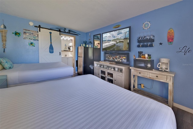 bedroom with a barn door, connected bathroom, and stainless steel refrigerator