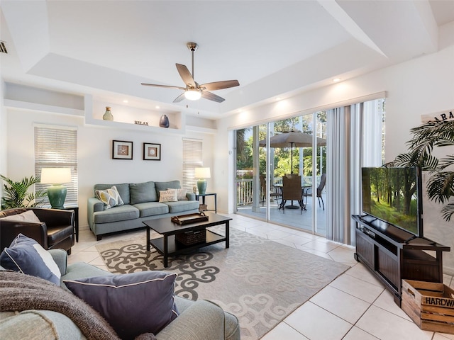 living room featuring a tray ceiling, ceiling fan, and light tile flooring