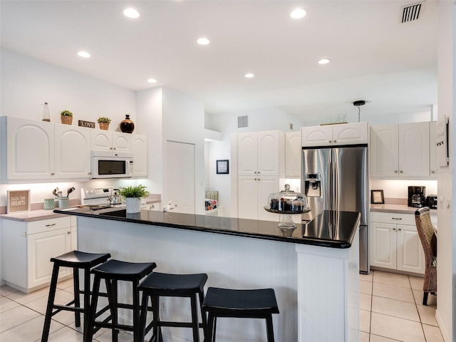 kitchen featuring a kitchen bar, a center island with sink, white appliances, and white cabinetry