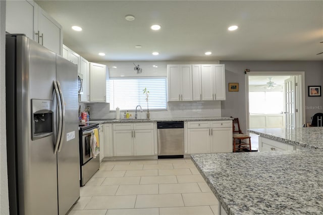 kitchen with appliances with stainless steel finishes, light tile flooring, backsplash, and white cabinetry