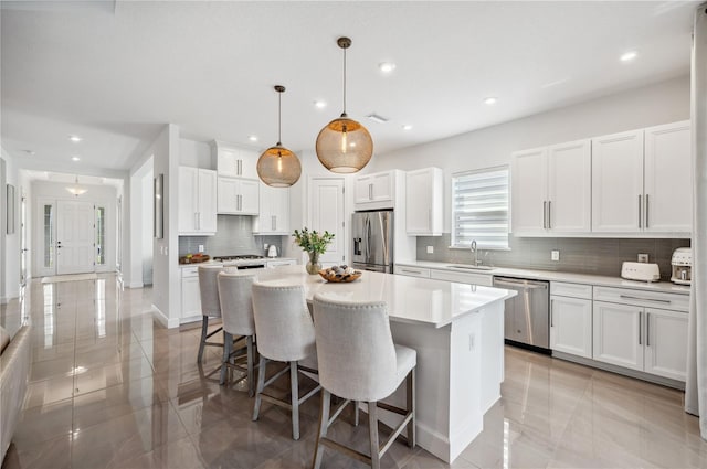 kitchen featuring decorative light fixtures, appliances with stainless steel finishes, sink, white cabinets, and a center island