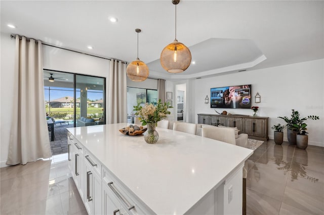 kitchen featuring decorative light fixtures, a tray ceiling, ceiling fan, light tile floors, and white cabinets