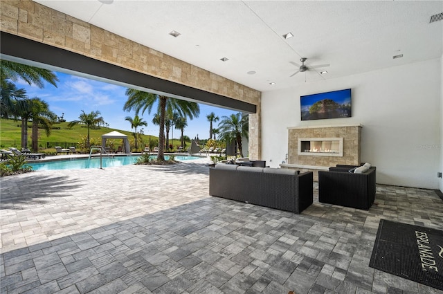 view of terrace with an outdoor living space with a fireplace and ceiling fan