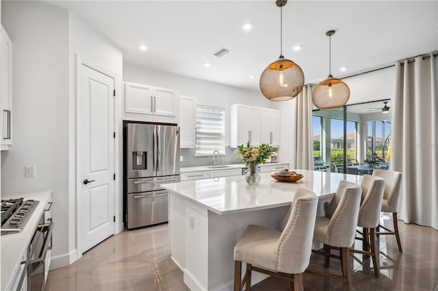 kitchen with hanging light fixtures, appliances with stainless steel finishes, light tile floors, white cabinets, and a center island