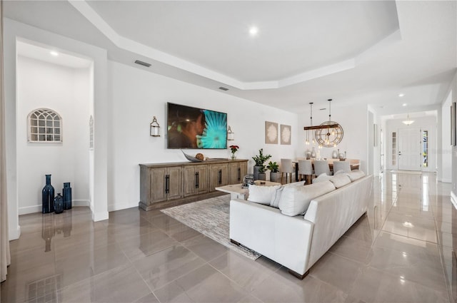 living room featuring an inviting chandelier, visible vents, a tray ceiling, and baseboards